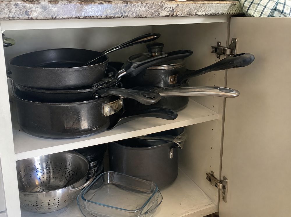 Kitchen cabinet crowded with pans and long handles