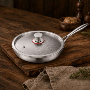 Hammered titanium frying pan with tempered glass lid and steam vent on a wooden board