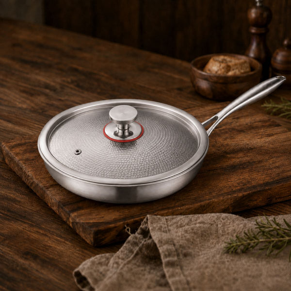 Hammered titanium frying pan with tempered glass lid and steam vent on a wooden board