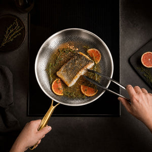 Searing a fish fillet with orange slices in the hammered titanium frying pan with gold handle