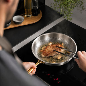 Searing meat with tongs in the hammered titanium frying pan with gold handle on an induction cooktop