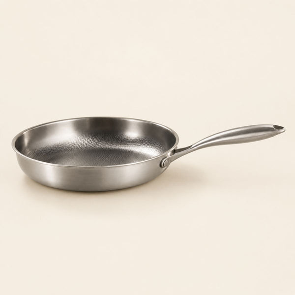 Hammered titanium frying pan, three-quarter view on a plain cream background