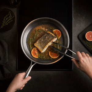 Overhead view of a fish fillet cooking with citrus and herbs in the hammered titanium pan