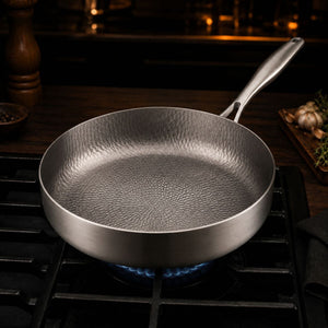 Empty deep titanium frying pan heating over a gas flame, hammered base visible
