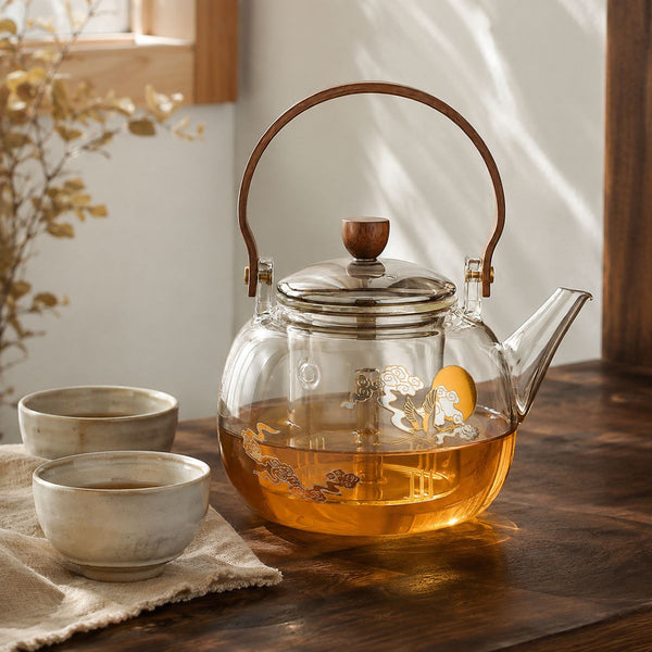 Hikari glass kettle filled with amber tea beside two stoneware cups
