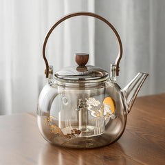 Hikari glass tea kettle with wooden handle and gold cloud motif on a table