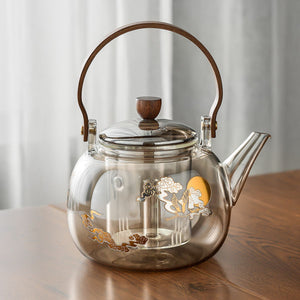Hikari glass tea kettle with wooden handle and gold cloud motif on a table