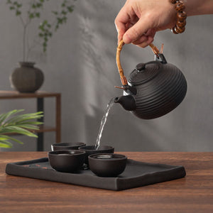 Tea poured from the Nagi matte black clay teapot into cups on the serving tray