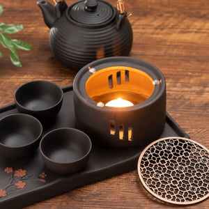 Lit tealight inside the Nagi tea warmer beside its metal top, cups and teapot