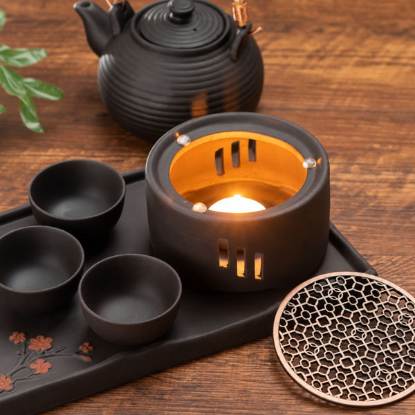 Lit tealight inside the Nagi tea warmer beside its metal top, cups and teapot