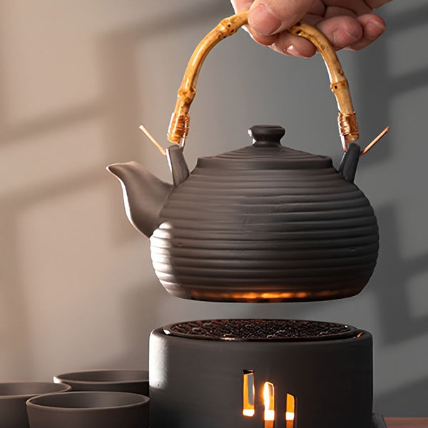Nagi matte black clay teapot lifted above its lit candle warmer