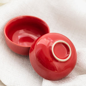 Red porcelain tea cup with its lid resting alongside on linen