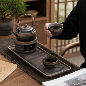 Hand holding a Renji tea cup beside the teapot on its warmer