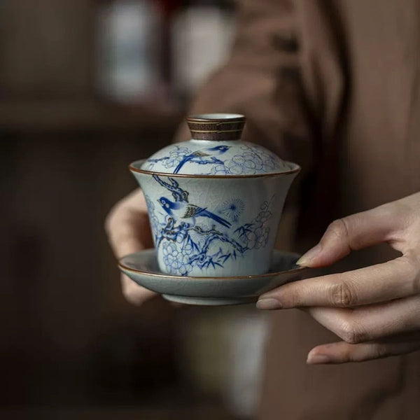Hands holding the Rui Ruyao ceramic gaiwan with magpie and plum blossom design